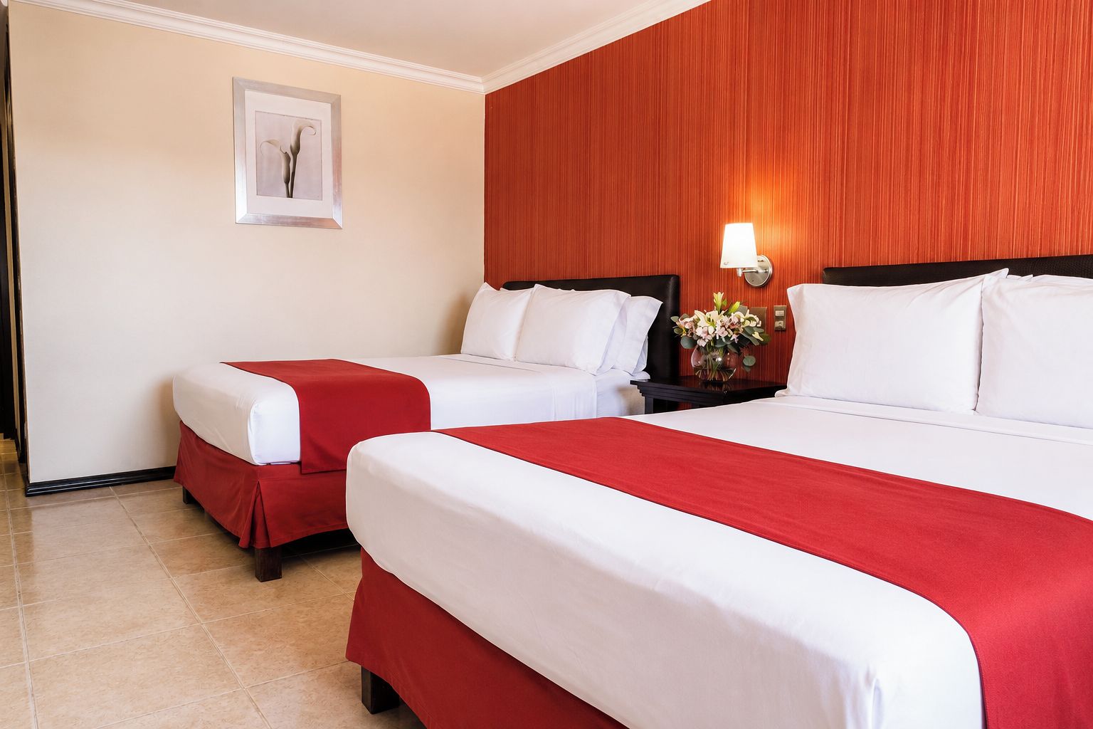 A hotel room with two beds, a nightstand with a lamp, and a framed picture on the wall.