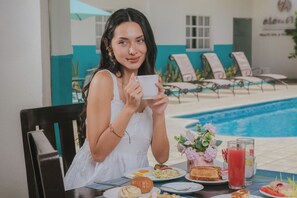 Una persona seduta a tavola con un pasto, una piscina e sedie a sdraio sullo sfondo.