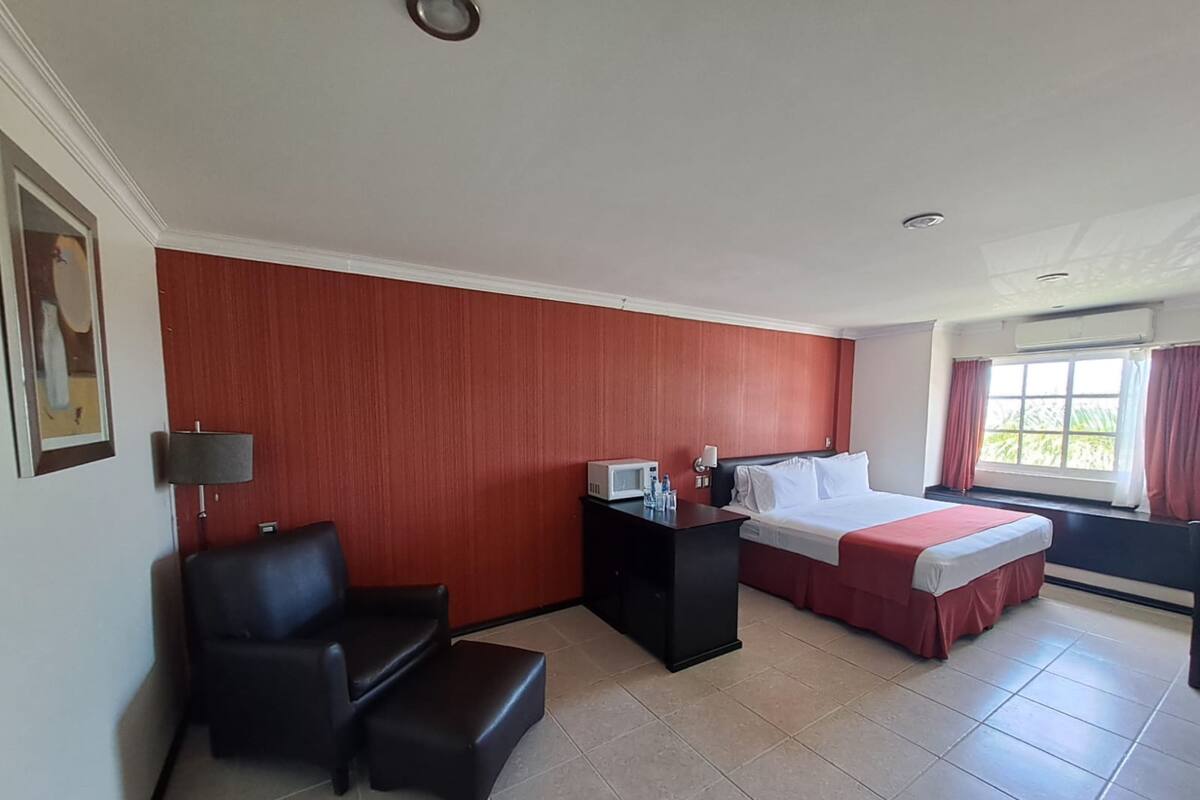 Camera d'albergo con un letto, una scrivania con lampada, una sedia e una finestra con tende.