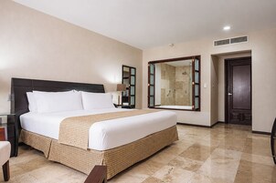 A hotel room with a large bed, a bathroom with a shower, and a door leading to another room.