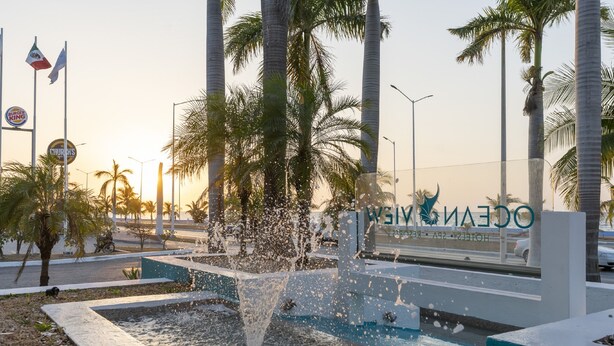 A fountain with water jets, palm trees, and flags. - Ocean View Hotel (Campeche)