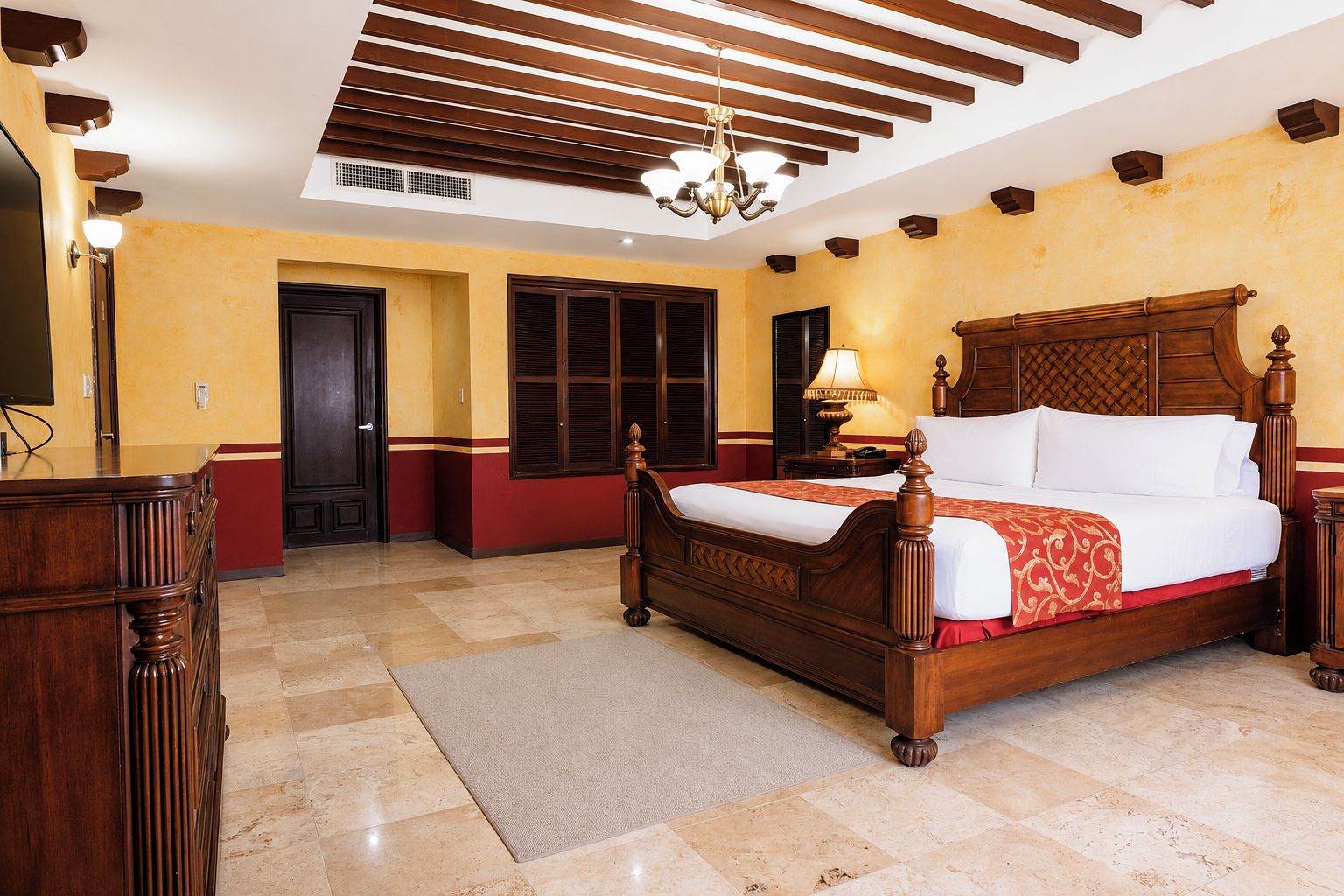 A hotel room with a large bed, a wooden headboard, a chandelier, and a desk with a lamp.