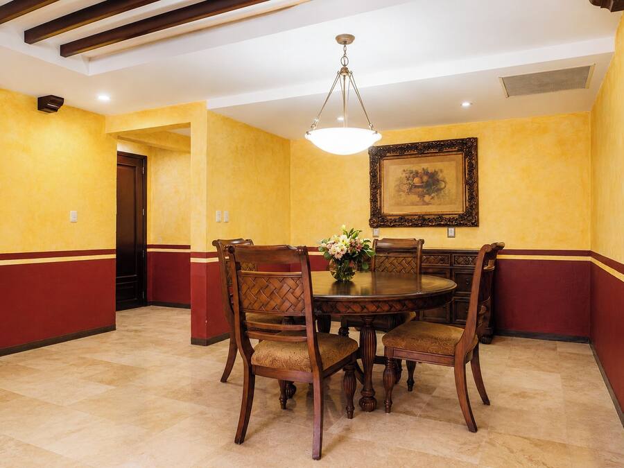A dining area with a round table, six wooden chairs, and a chandelier.