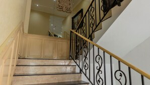 Una scala con ringhiere nere e gradini beige che conduce a un muro specchiato e un elemento decorativo a soffitto.