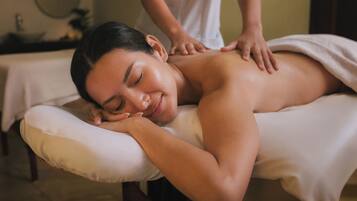 A person receiving a back massage on a massage table in a room with a bed and a round mirror on the wall.
