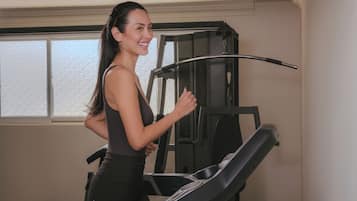 Una mujer usando una caminadora en una habitación con ventana y una máquina de ejercicio montada en la pared.