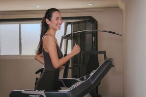 Una donna utilizza un tapis roulant in una stanza con una finestra e un'attrezzatura ginnastica fissata al muro.
