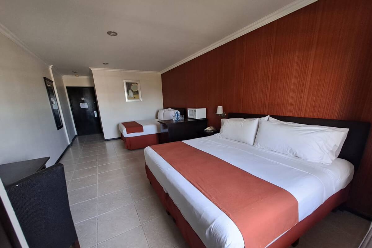 Camera d'albergo con un ampio letto, una scrivania e una sedia. Si trova un forno a microonde sulla scrivania e un telefono sul comodino.