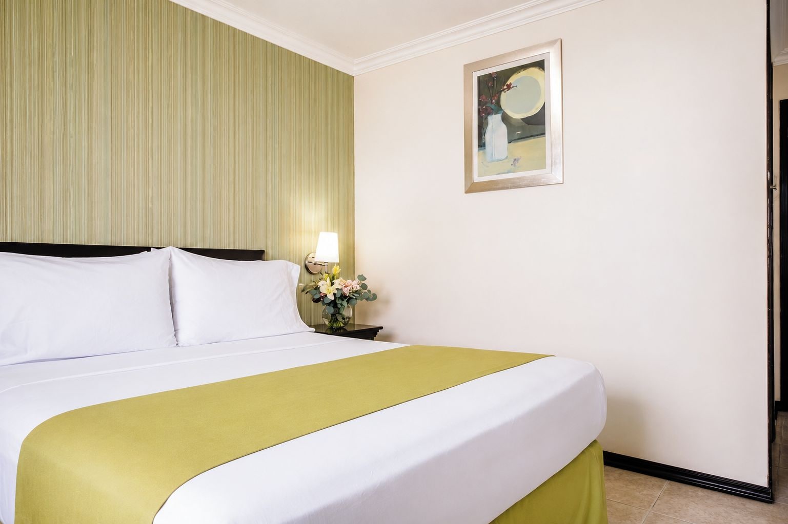 Habitación de hotel con una cama grande, una mesita de noche con lámpara y un cuadro enmarcado en la pared.