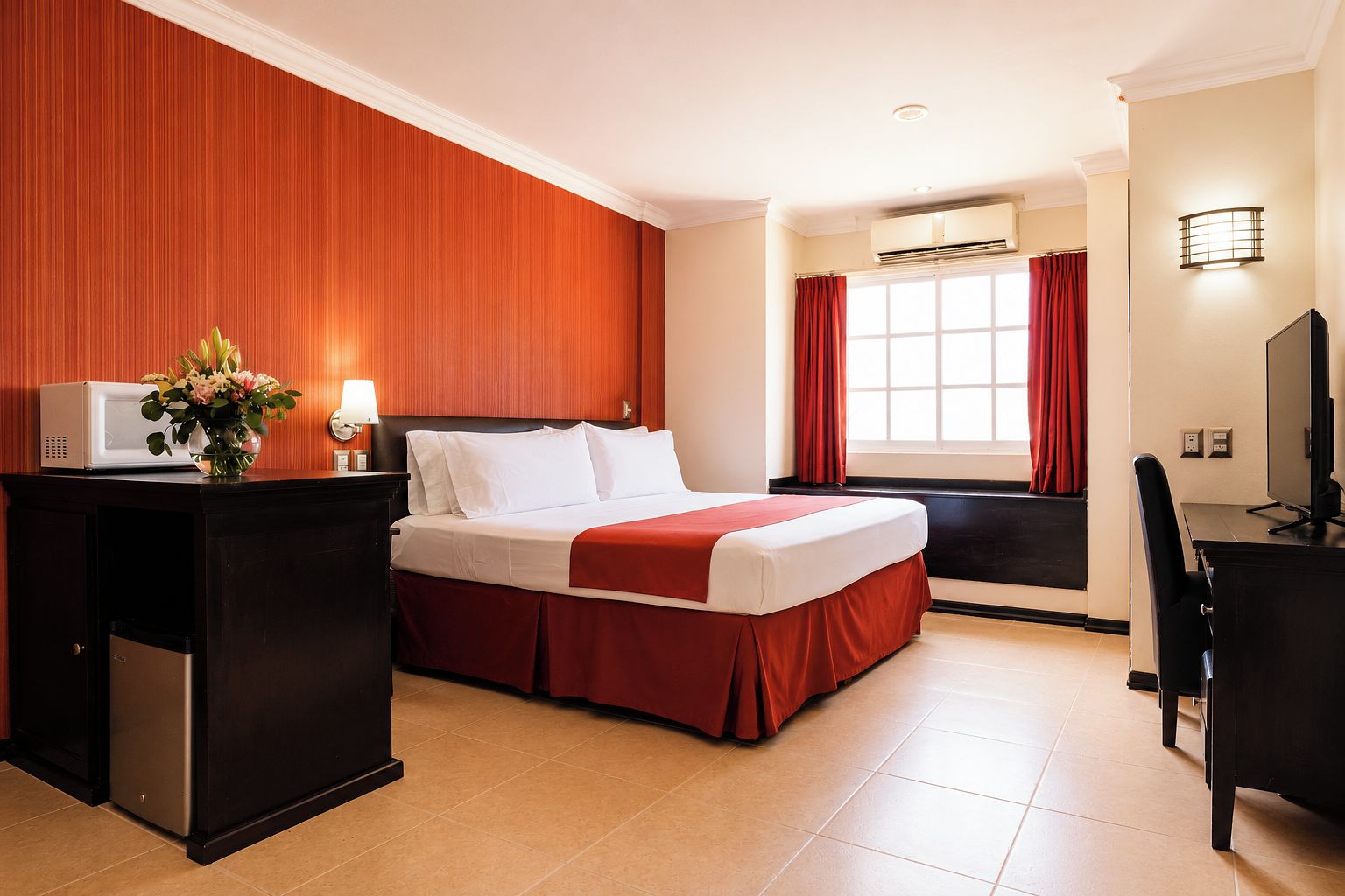 A hotel room with a bed, a desk, a television, and a window with curtains.