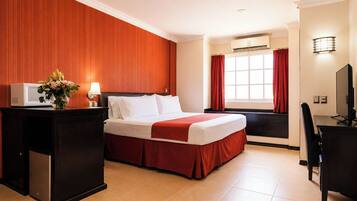 Quarto de hotel com cama, escrivaninha, televisão e janela com cortinas.