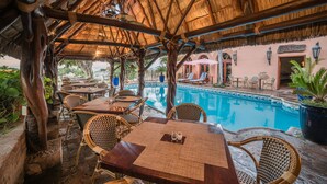 An outdoor pool area with thatched roof seating and tables, surrounded by lush greenery. - Hotel Posada del Hidalgo by Balderrama Hotel Collection (El Fuerte)
