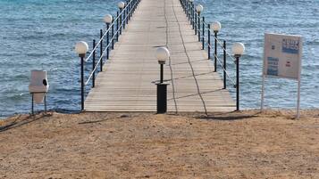 Un muelle de madera se extiende hacia el mar, con barandas y faroles, que conduce a una costa distante.