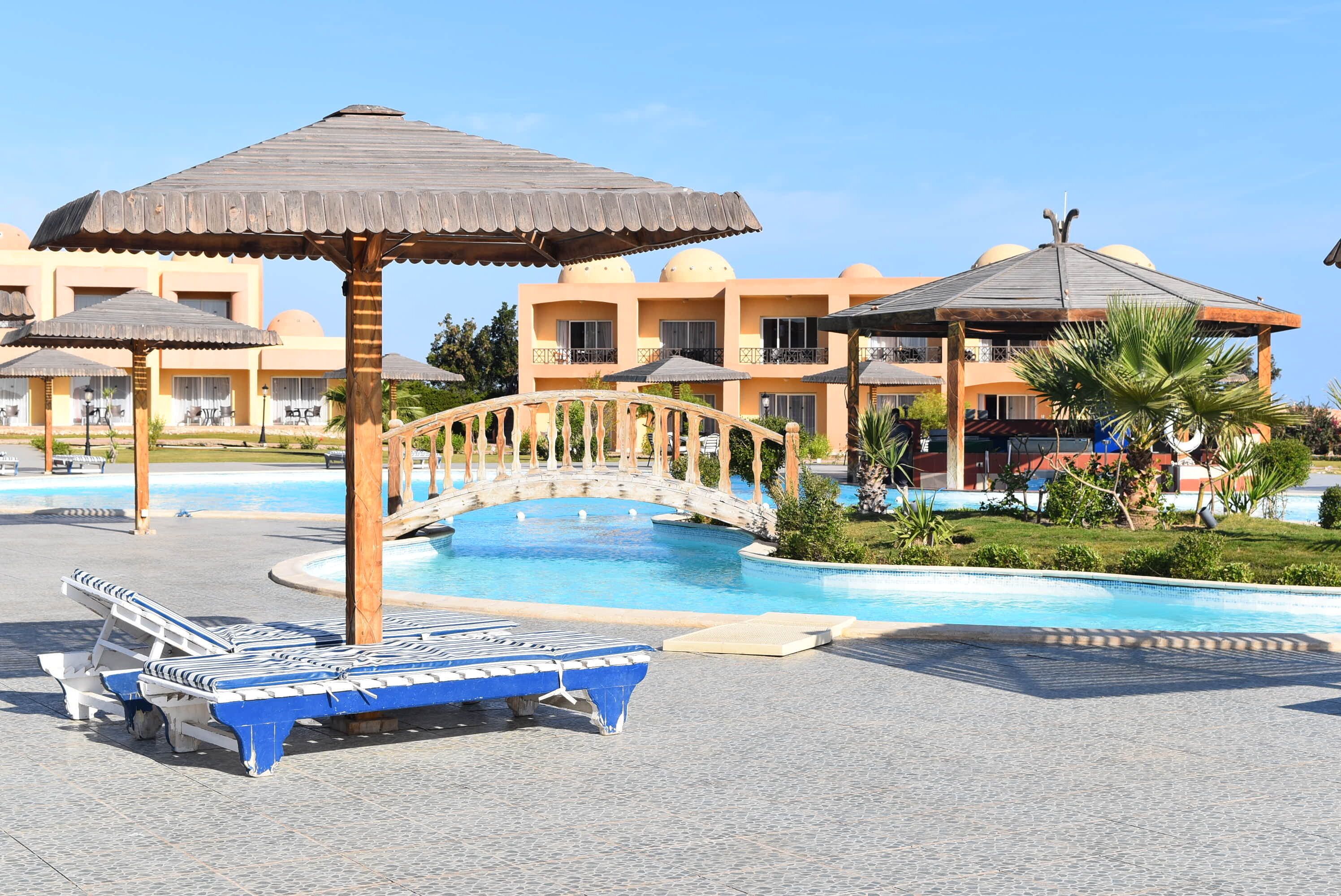 Area piscina con lettini, un ponte e un edificio con balconi.
