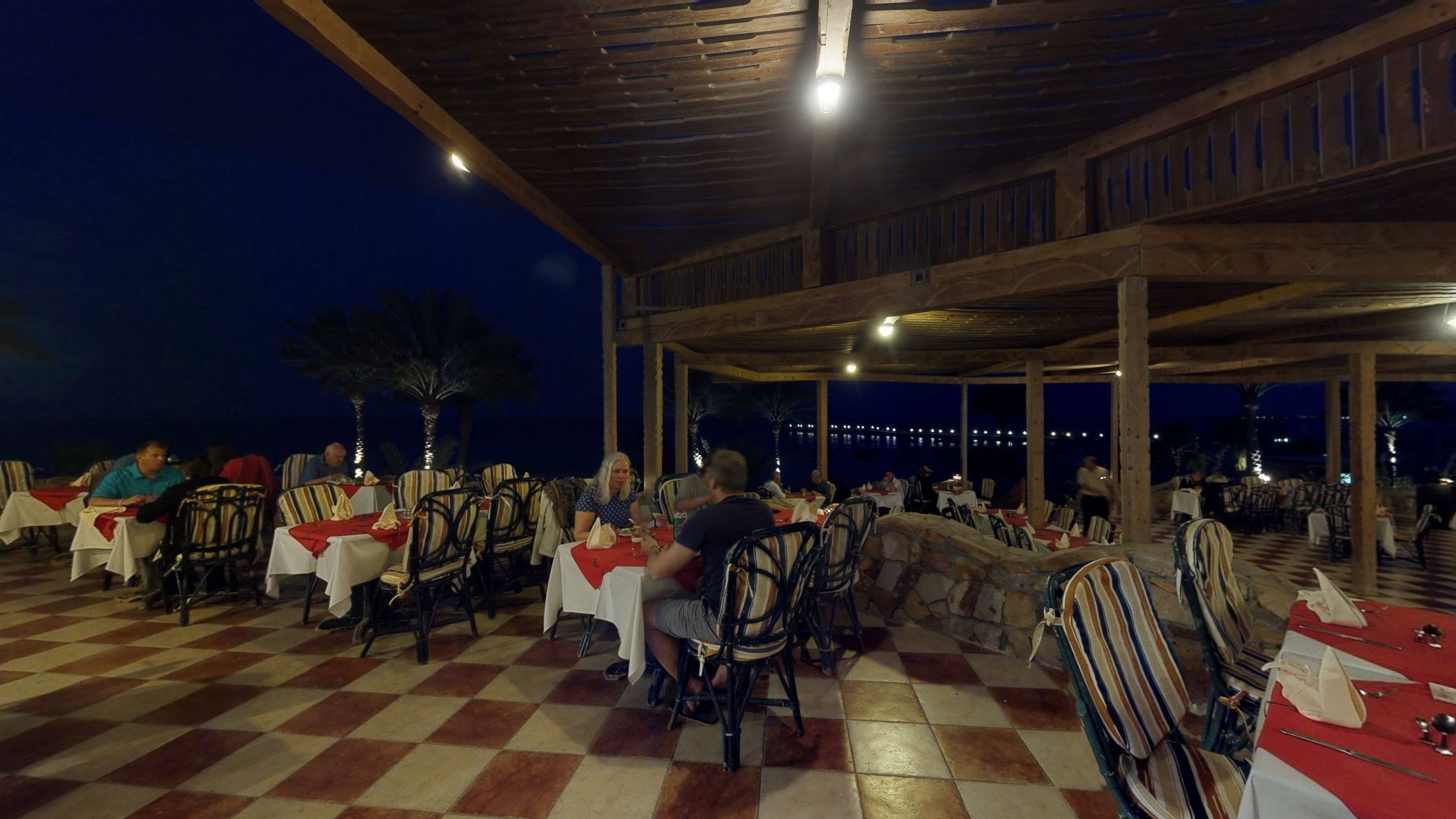 An outdoor dining area with tables and chairs, a checkered floor, and a view of the night sky.