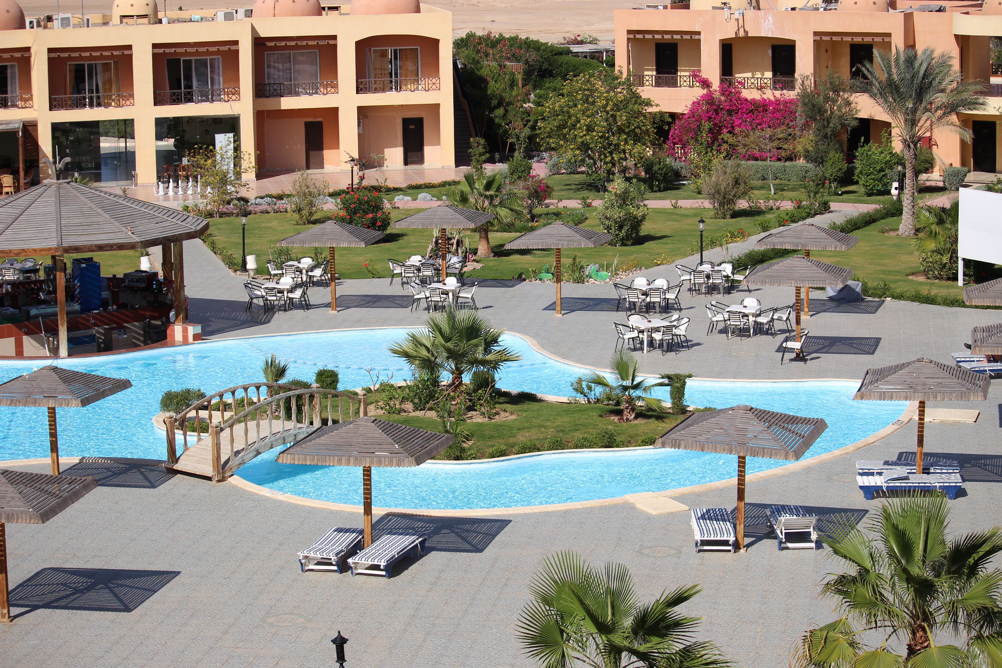 A resort with a swimming pool, sun loungers, umbrellas, and a covered seating area.