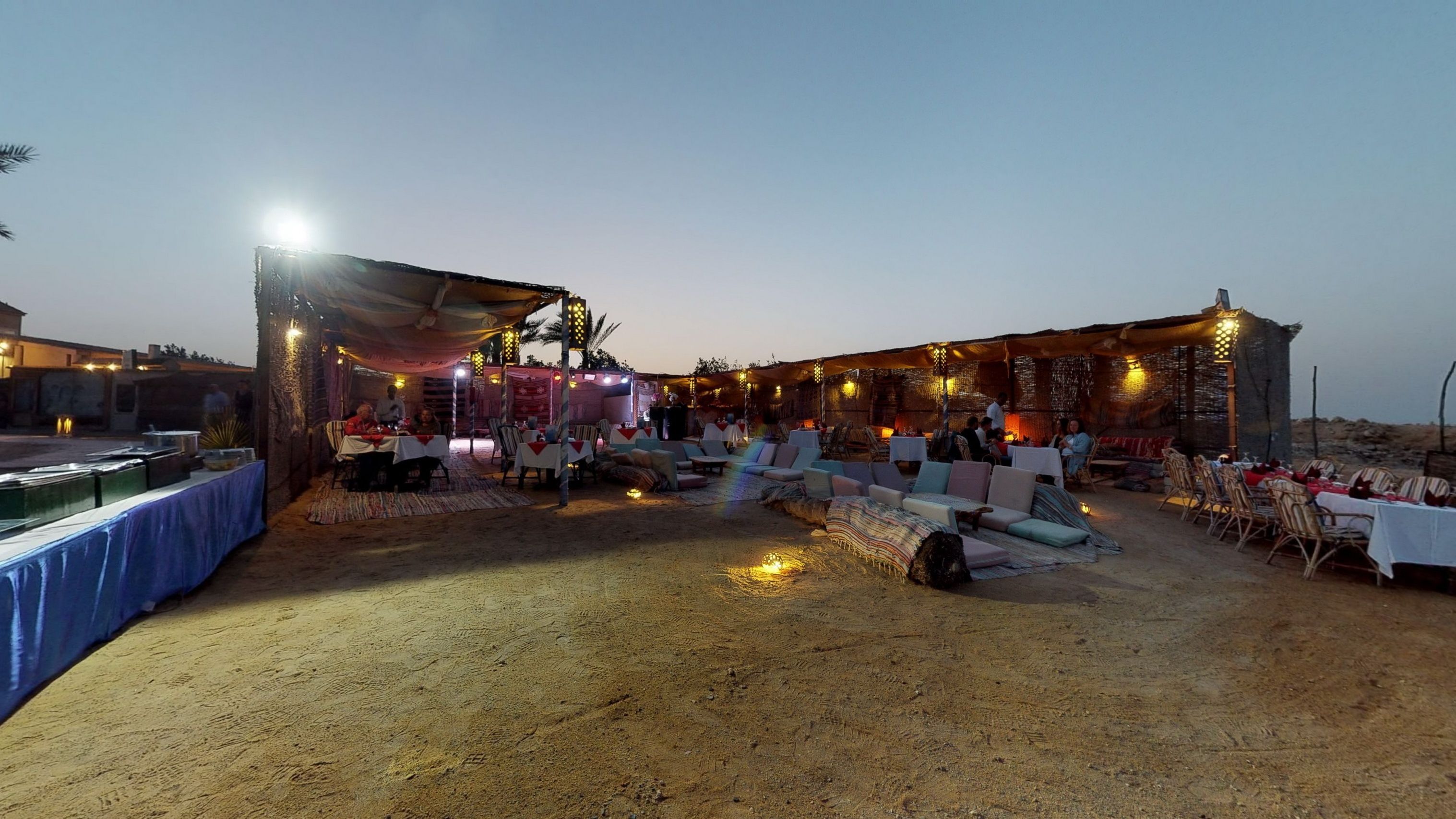 An outdoor dining area with tables and chairs, a stage, and string lights.