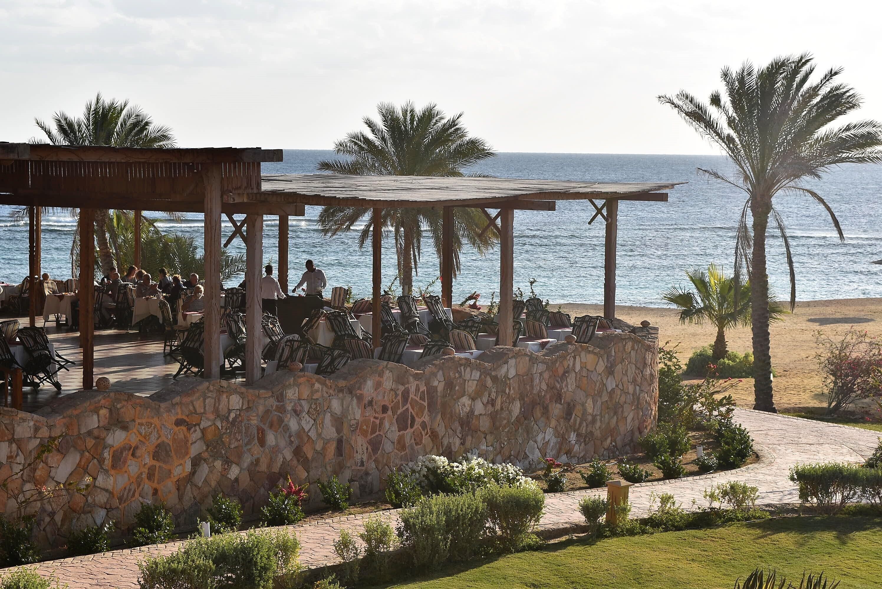 Un restaurante frente a la playa con terraza, paredes de piedra y palmeras.