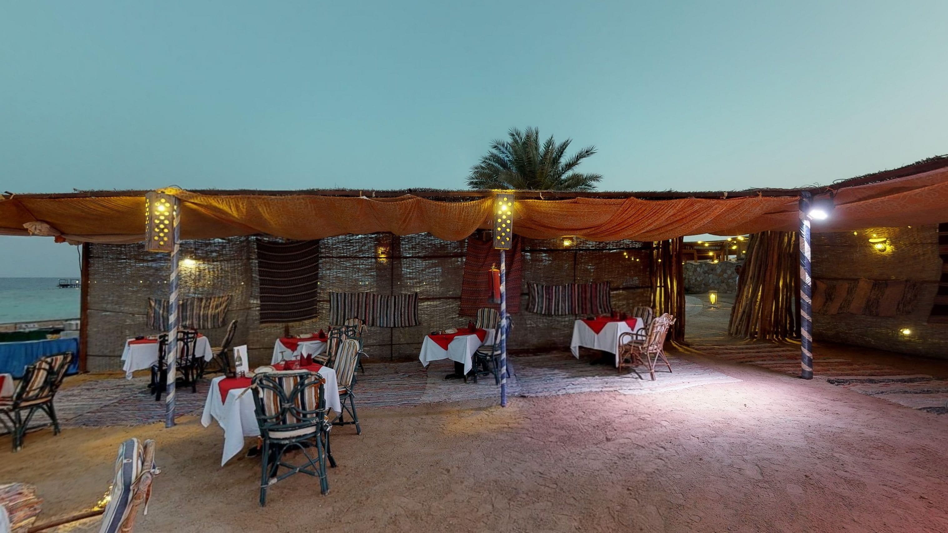An outdoor dining area with tables and chairs, a beach view, and string lights.