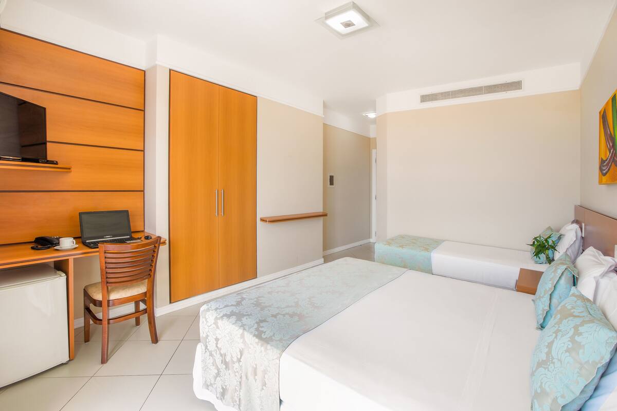 Ein Hotelzimmer mit Bett, Schreibtisch mit Laptop, Stuhl und Kleiderschrank.