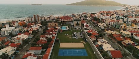 An aerial view of a coastal town with a prominent tennis court, residential buildings, and a beach in the background.