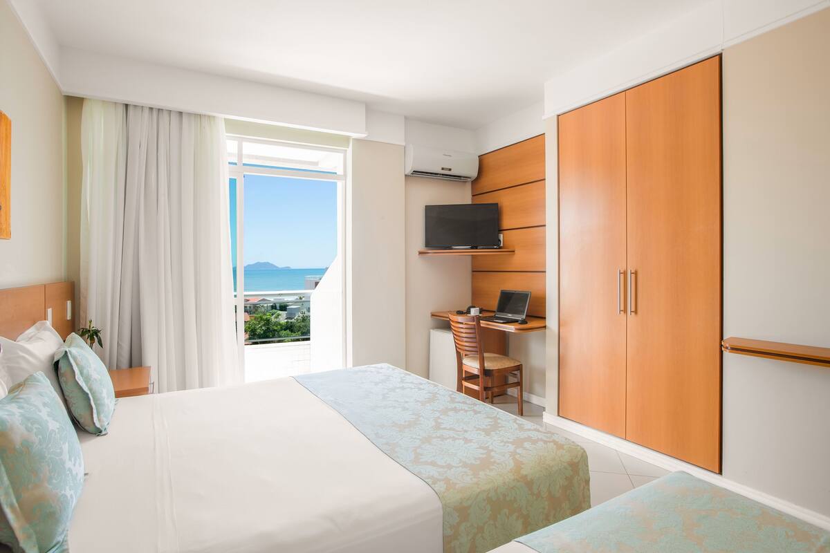 Ein Hotelzimmer mit einem Bett, einem Schreibtisch mit einem Laptop, einem Fernseher und einem Kleiderschrank.