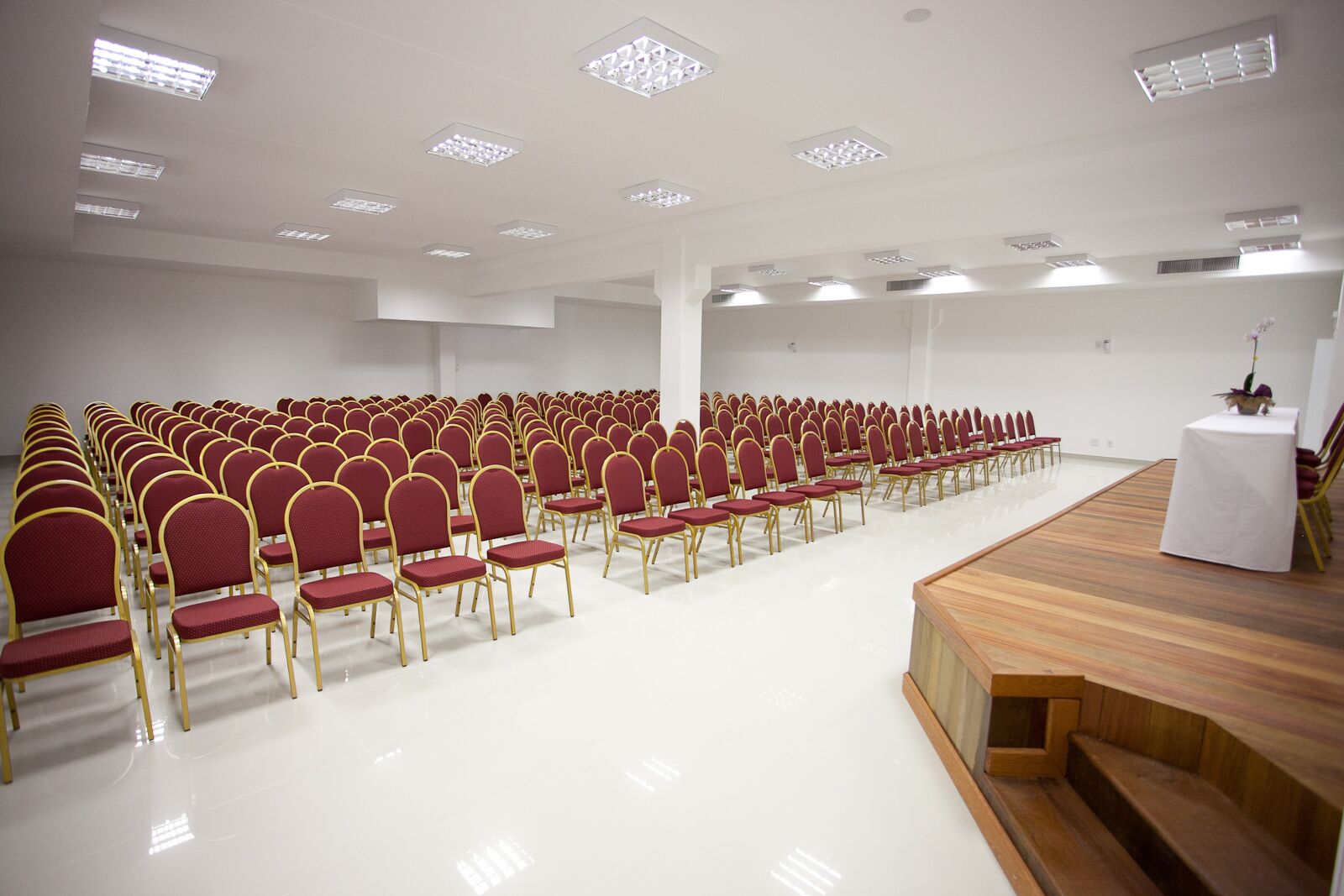 A conference room with rows of red chairs and a wooden stage.