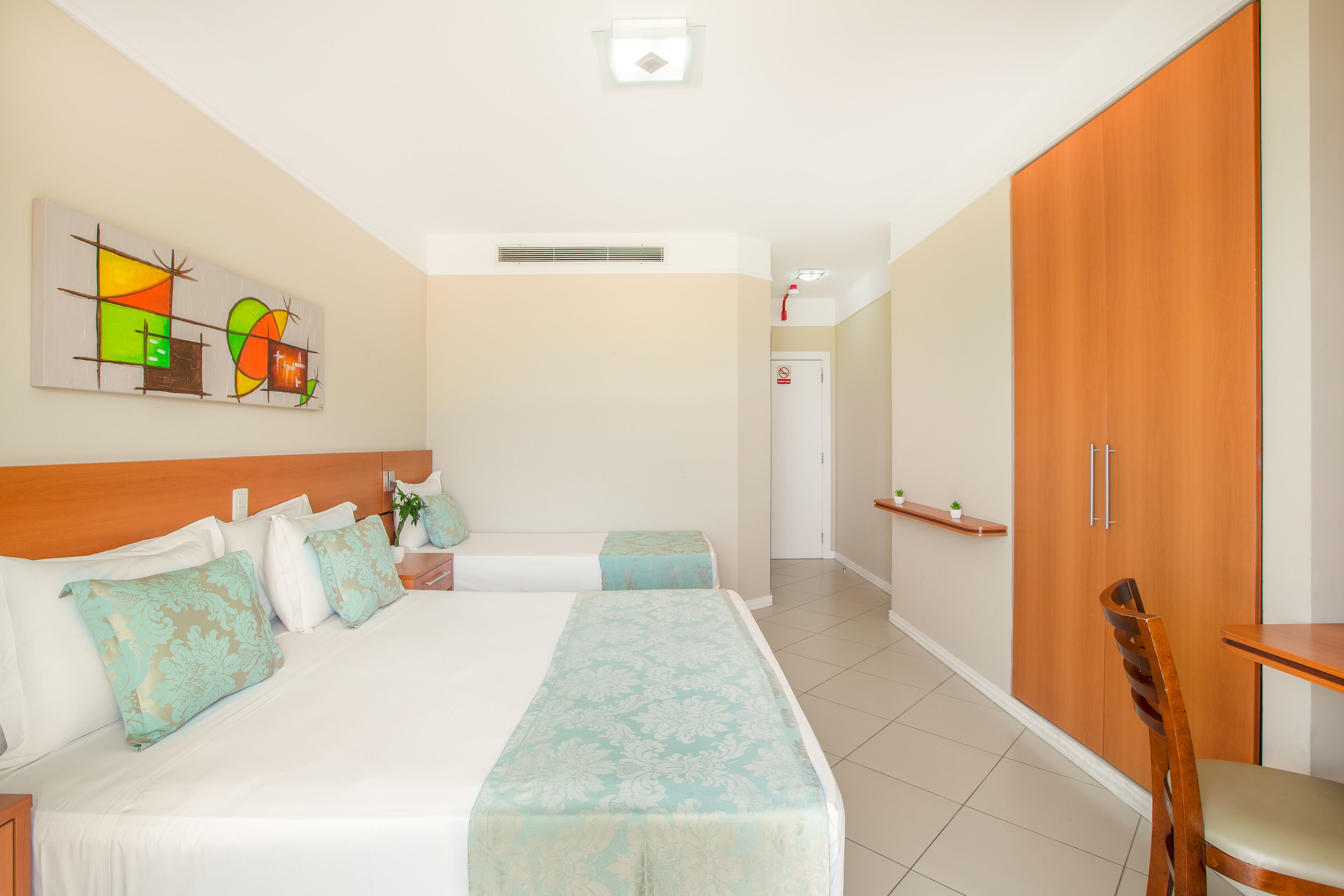Una habitación de hotel con una cama grande, un armario de madera, una mesita pequeña y una silla.