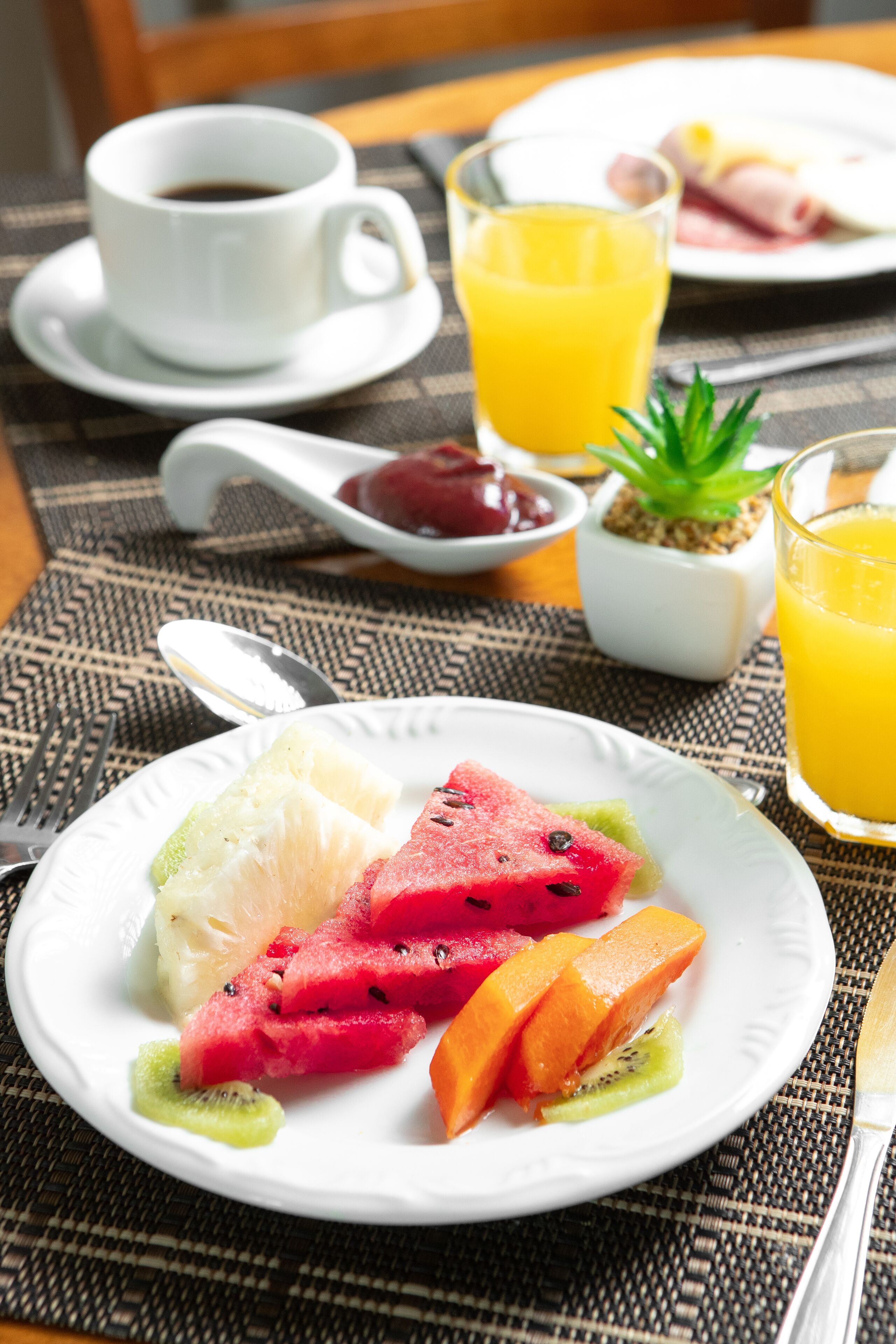 Un desayuno con una fuente de fruta, una taza de café y un vaso de jugo de naranja sobre una mesa.