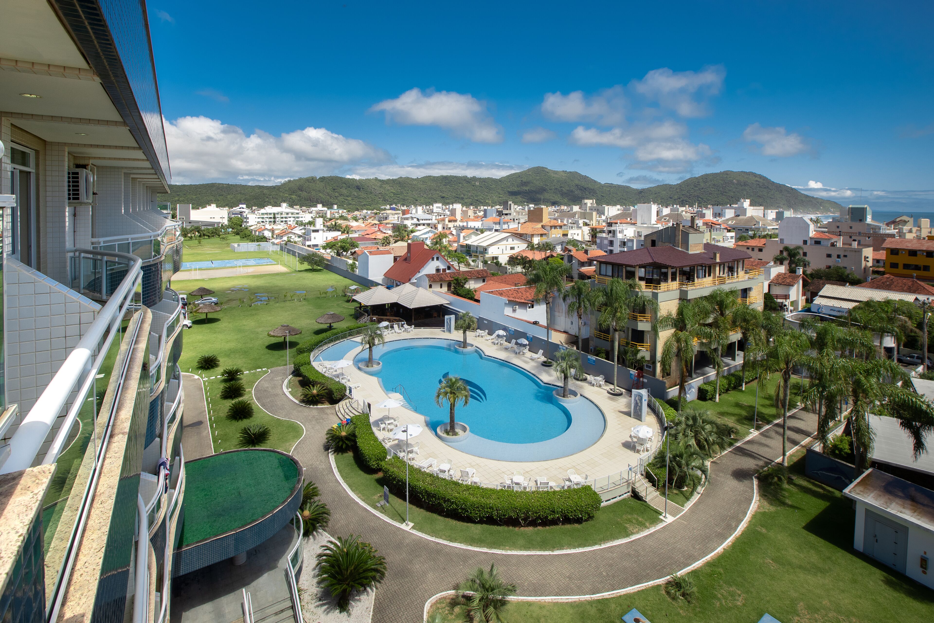 A resort with a large pool, a well-maintained lawn, and a view of the surrounding town and mountains.
