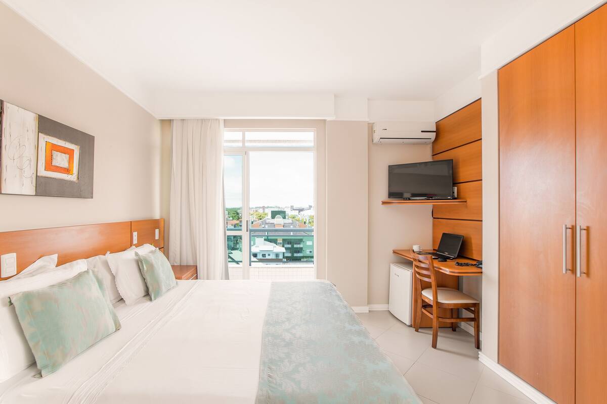 Ein Hotelzimmer mit einem Bett, einem Schreibtisch mit einem Laptop, einem Fernseher und einem Kleiderschrank.