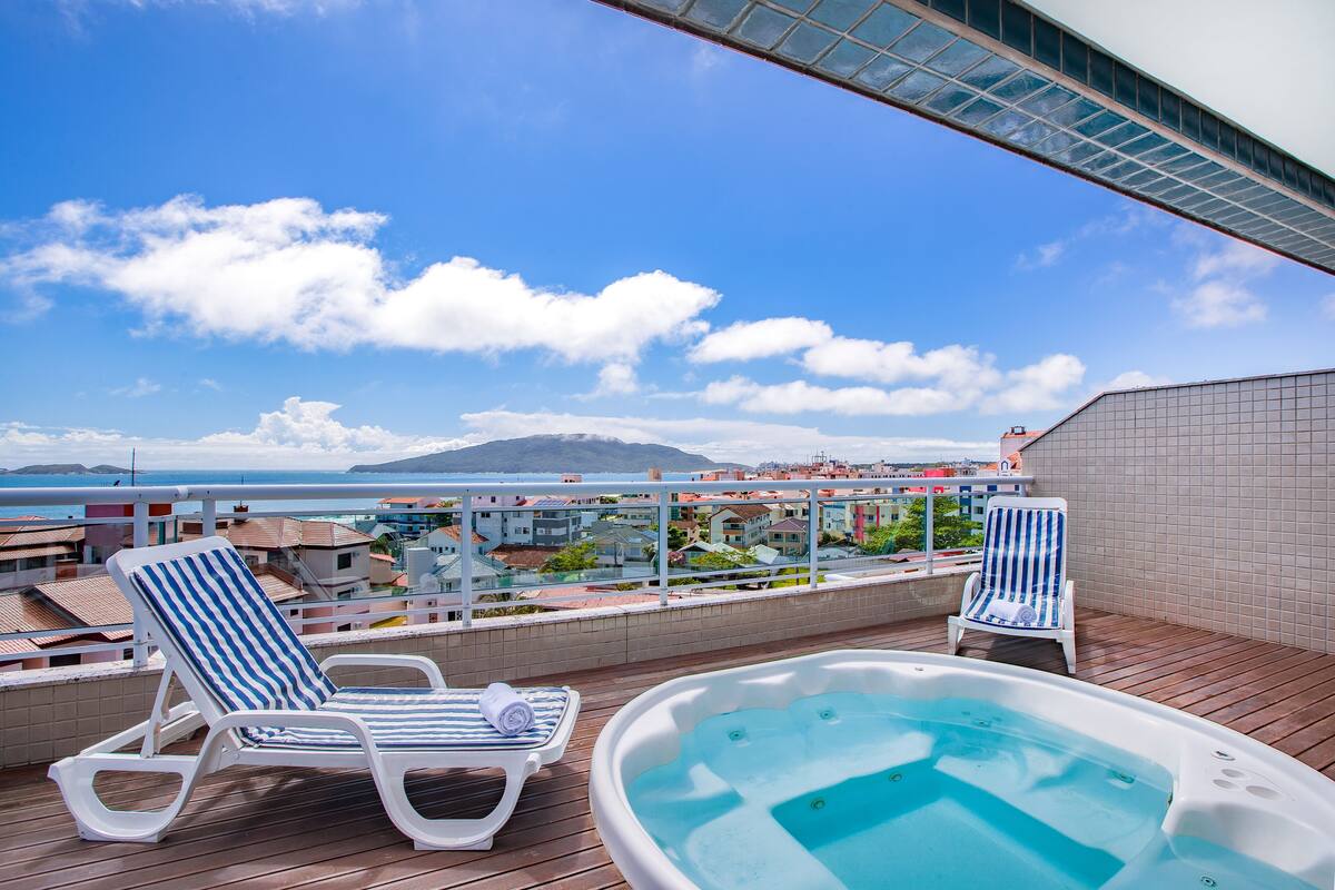 Eine Dachterrasse mit Whirlpool, zwei gestreiften Liegestühlen und Blick auf das Meer und die Gebäude.