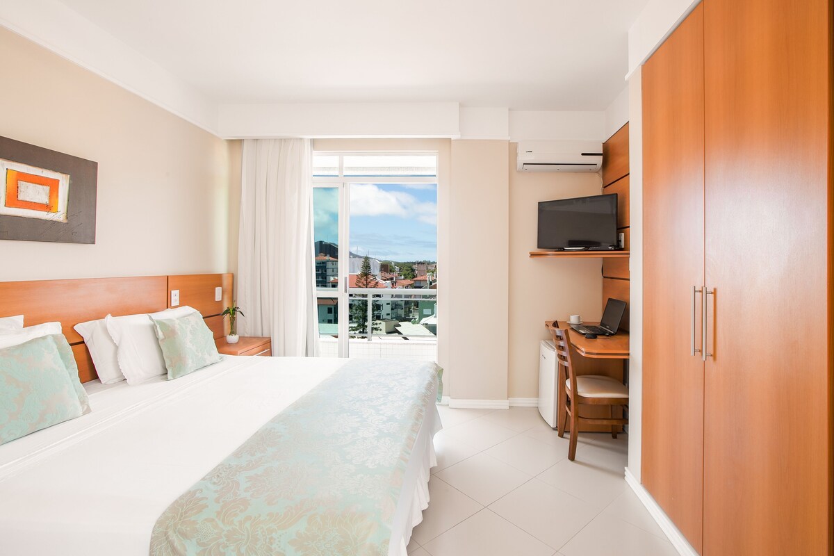 Een hotelkamer met een bed, een bureau met een laptop, een televisie en uitzicht op de stad.