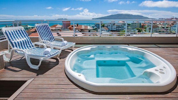 A deck with two striped lounge chairs and a hot tub. - Oceania Park Hotel Spa & Convention Center by RB Hotelaria (Florianópolis)