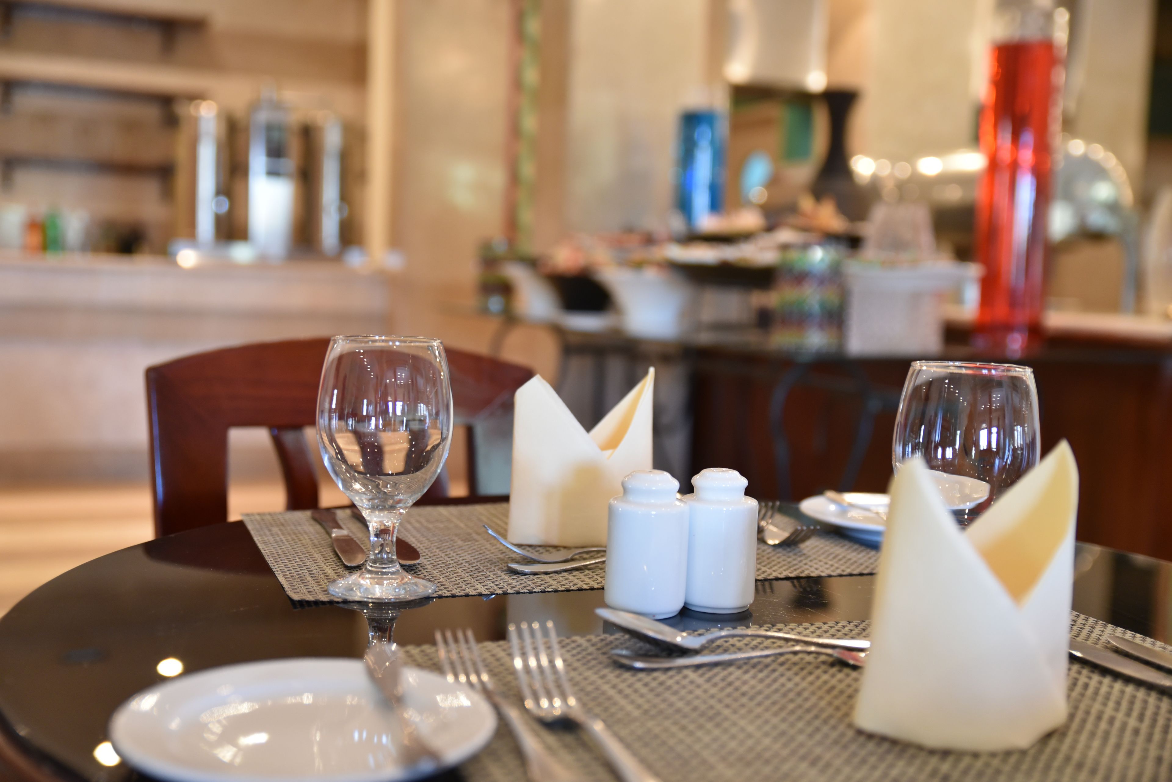 A dining table set with a wine glass, salt and pepper shakers, folded napkins, and cutlery.