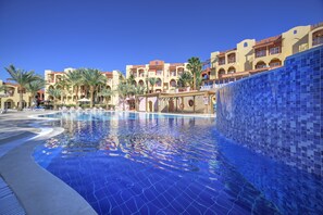 A swimming pool with tiled walls and a clear blue water surface, surrounded by palm trees and hotel buildings with balconies. - Marina Plaza Hotel, Tala Bay (Aqaba)