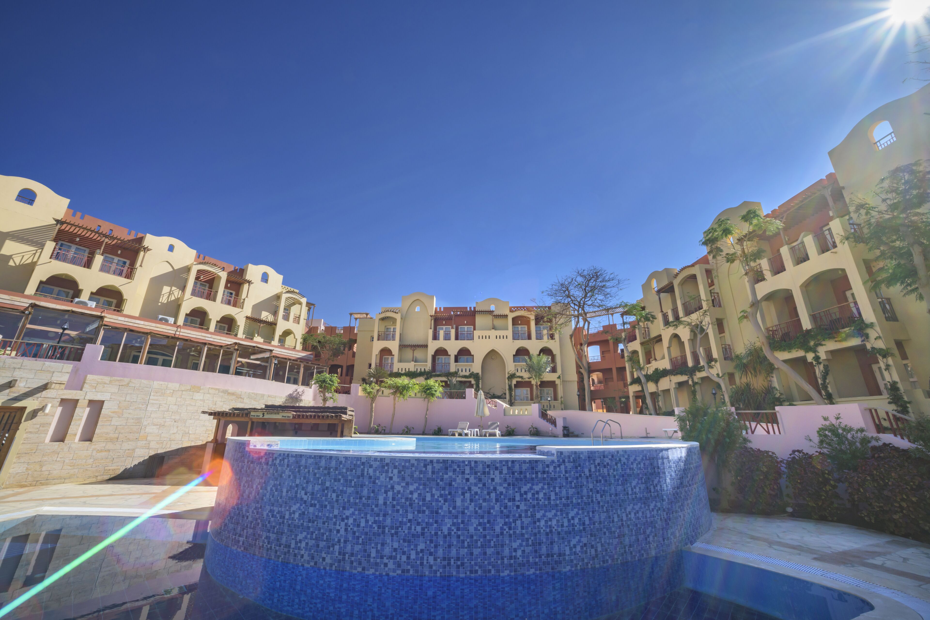 A hotel courtyard with a swimming pool, multiple balconies, and a clear blue sky.