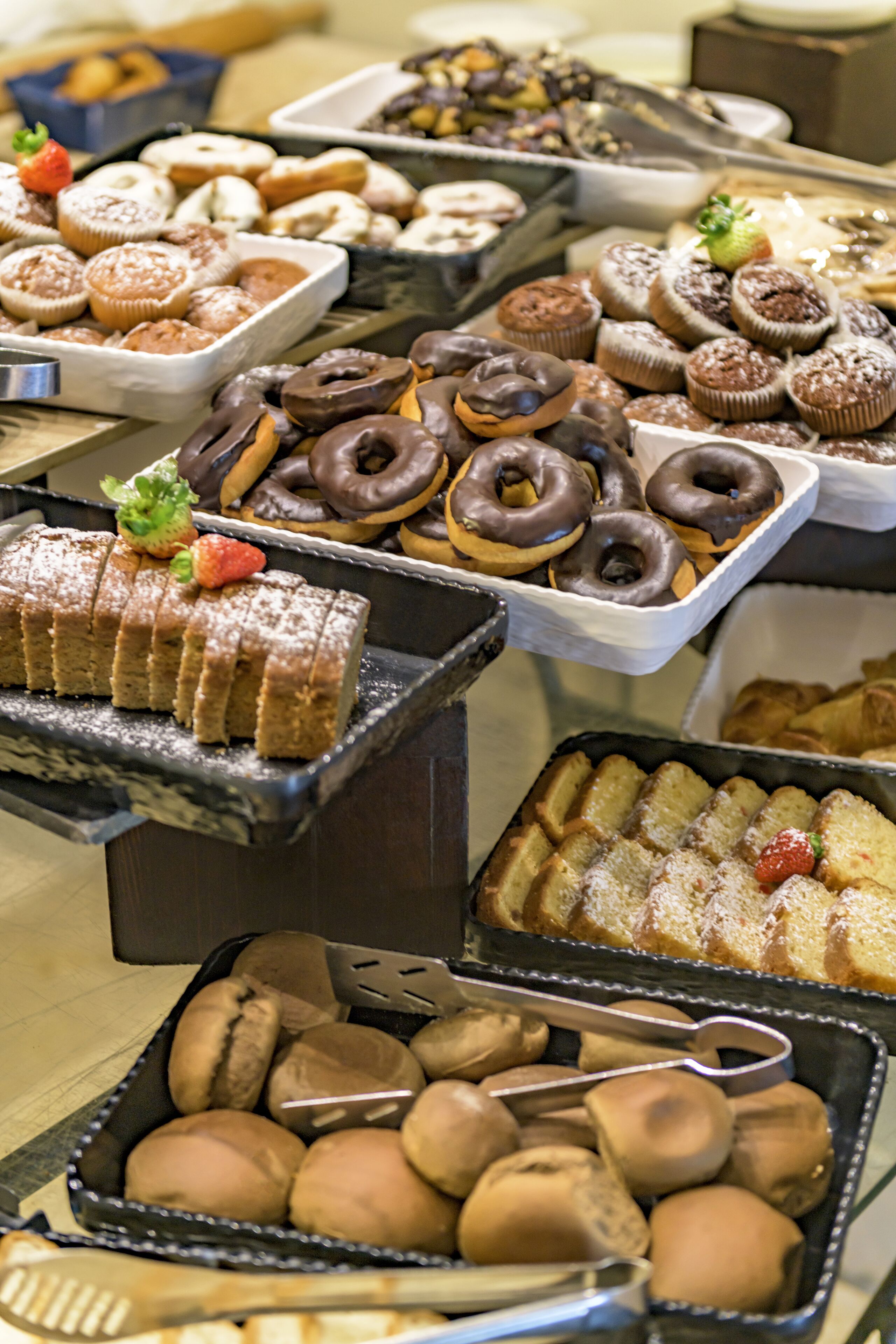 A variety of baked goods including donuts, muffins, and pastries displayed on trays.