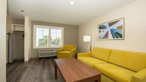 Una habitación con sofá amarillo, mesa de madera, ventana con persianas, radiador y un cuadro de rascacielos.