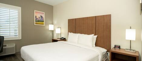 A hotel room with a large bed, two bedside tables with lamps, a chair, and a window with blinds.