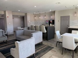 Un área de estar moderna con sofás grises, una mesa de comedor y una cocina con barra.