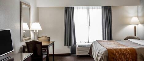 A hotel room with a bed, a desk with a chair, a TV, and a mirror.
