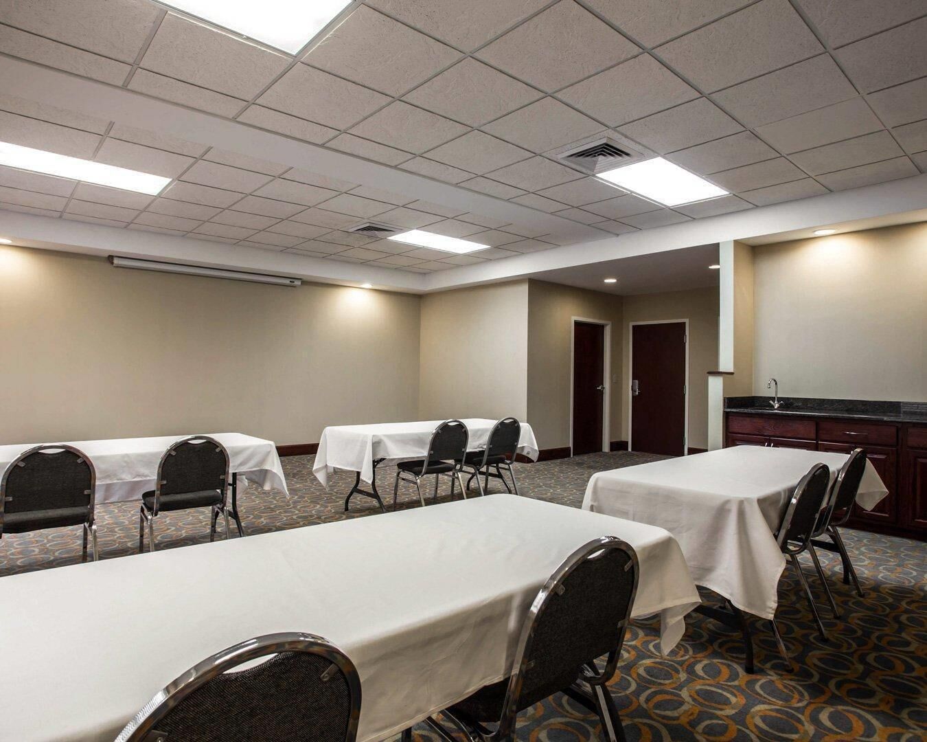 A conference room with tables and chairs, a kitchenette, and a door leading to another room.
