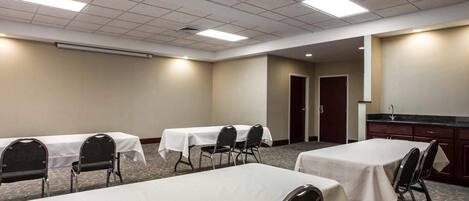 A conference room with tables and chairs, a kitchenette, and a door leading to another room.
