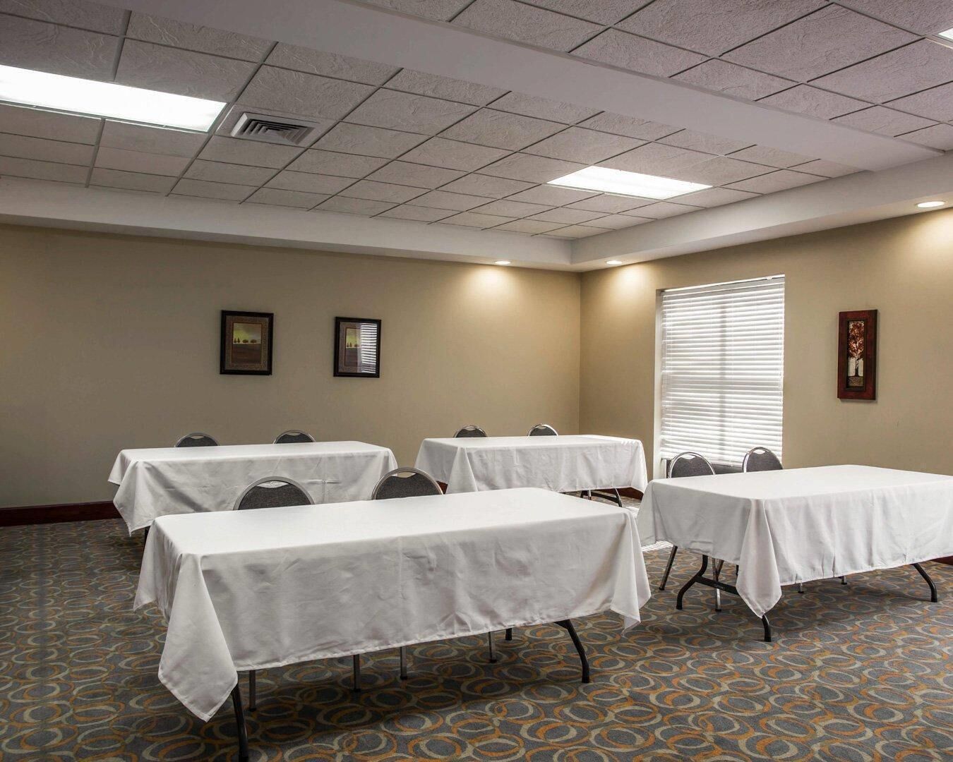 A conference room with four tables, a patterned carpet, and a window with blinds.