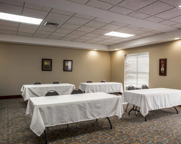 A conference room with four tables, a patterned carpet, and a window with blinds.