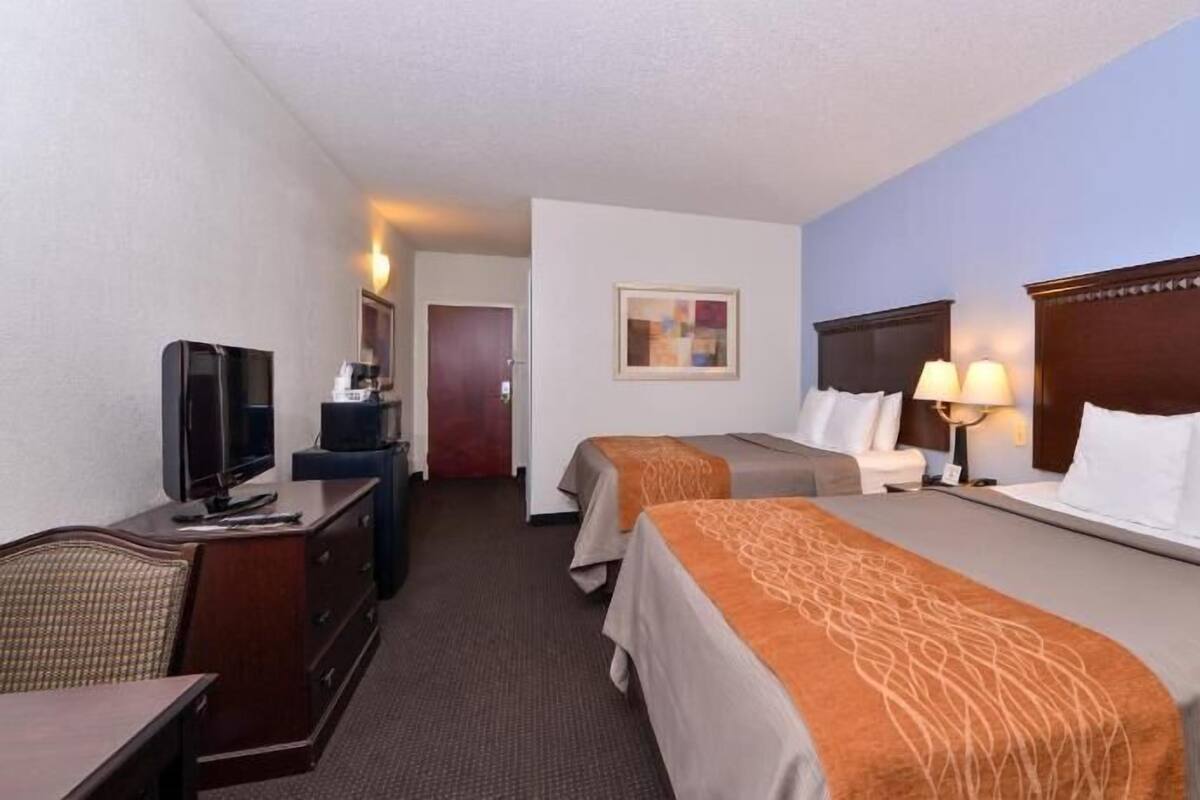 Habitación de hotel con dos camas, un escritorio con televisor, cómoda y un cuadro en la pared.