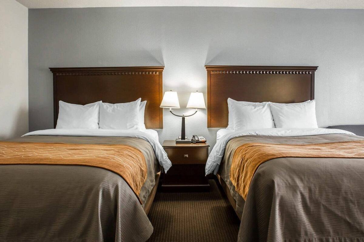 Una habitación de hotel con dos camas, una mesita de noche con lámparas y suelo alfombrado.