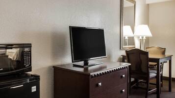 Habitación de hotel con televisión de pantalla plana en una cómoda, microondas, escritorio con silla y lámpara.