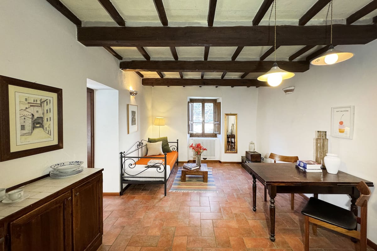 A cozy room with a bed, a table, and a chair. There is a window with a view of the outside.